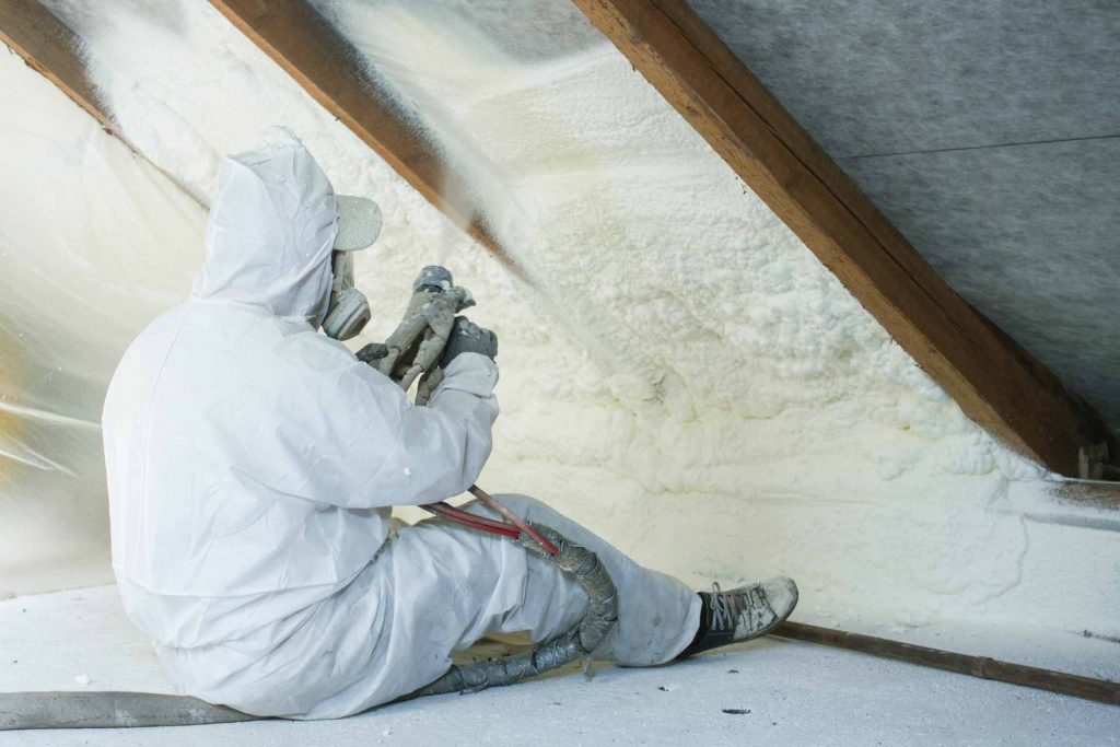 Worker spraying foam insulation in an attic